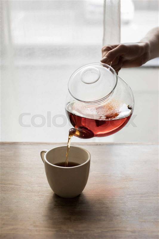 Cropped view of person pouring tea into cup, stock photo