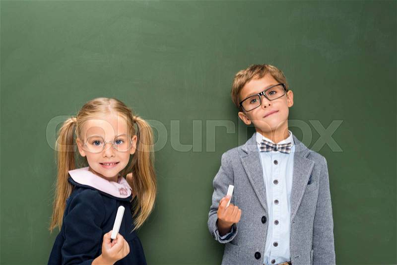 Adorable pupils with chalk pieces next to blackboard, stock photo