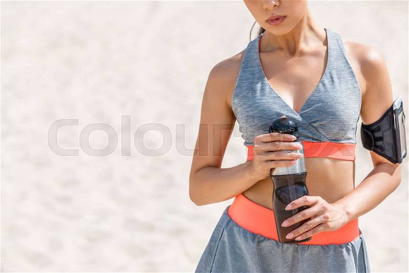 Cropped view of sportswoman with sport bottle and sport armband for smartphone, stock photo