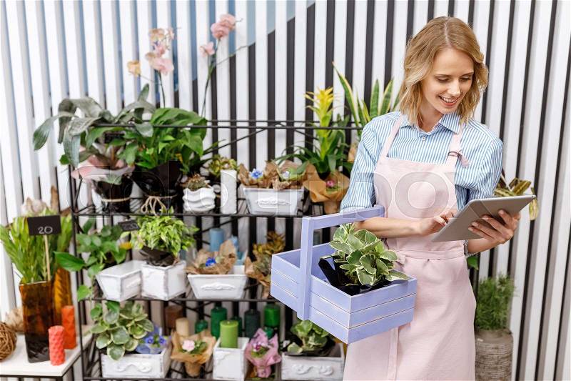 Smiling young florist using digital tablet while working in flower shop, stock photo