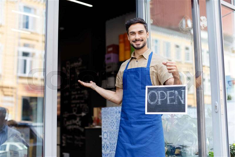 Small business owner holding open sign and smiling at camera, stock photo
