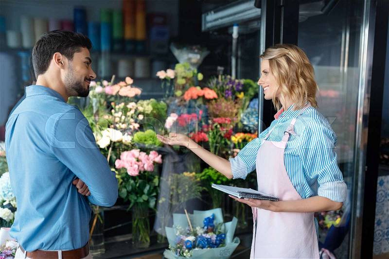 Young female florist and handsome male client smiling each other in flower shop, stock photo