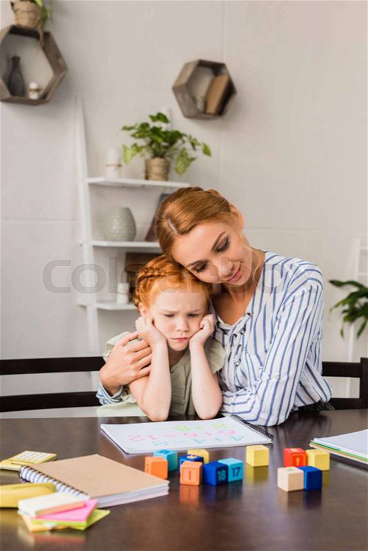Mother embracing daughter sad about math homework, stock photo