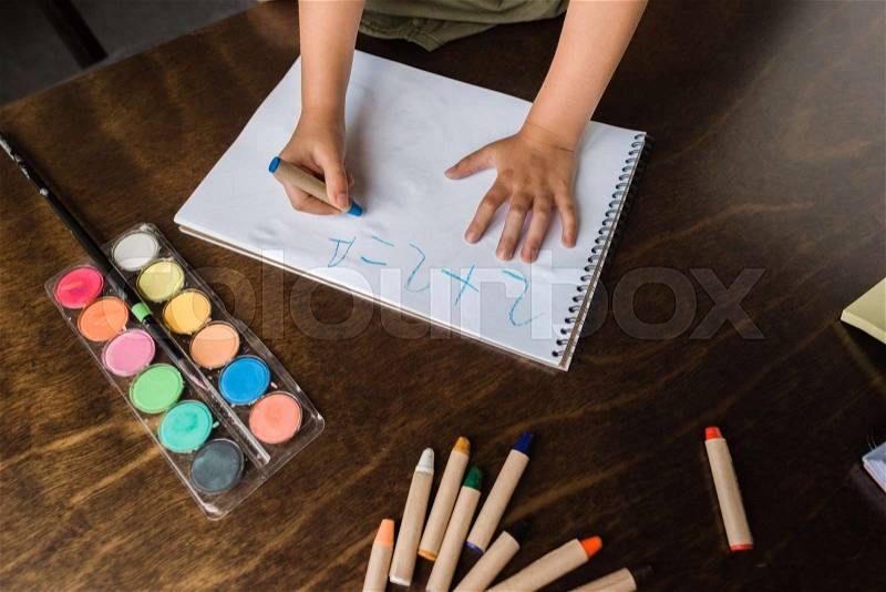 Cropped shot of child writing math exercise with crayon in album, stock photo