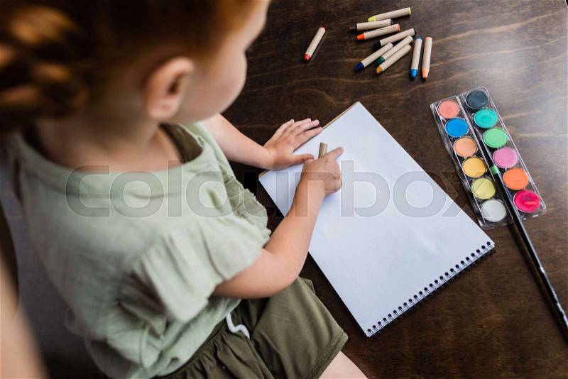 Top view of little girl drawing in album with color pencils, stock photo