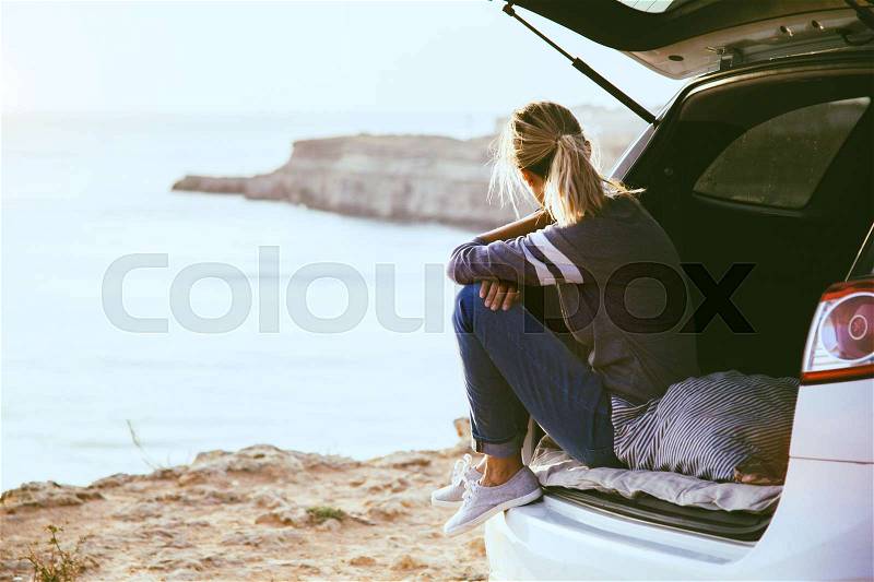 Woman relaxing inside car trunk and watching on sea. Fall trip in sunset. Freedom travel concept. Autumn weekend, stock photo