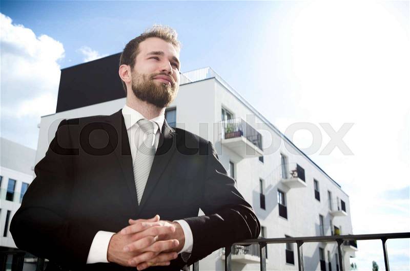 Relaxed businessman standing on balcony of his apartment. businessman outdoor friendly caucasian suit balcony city apartment concept, stock photo