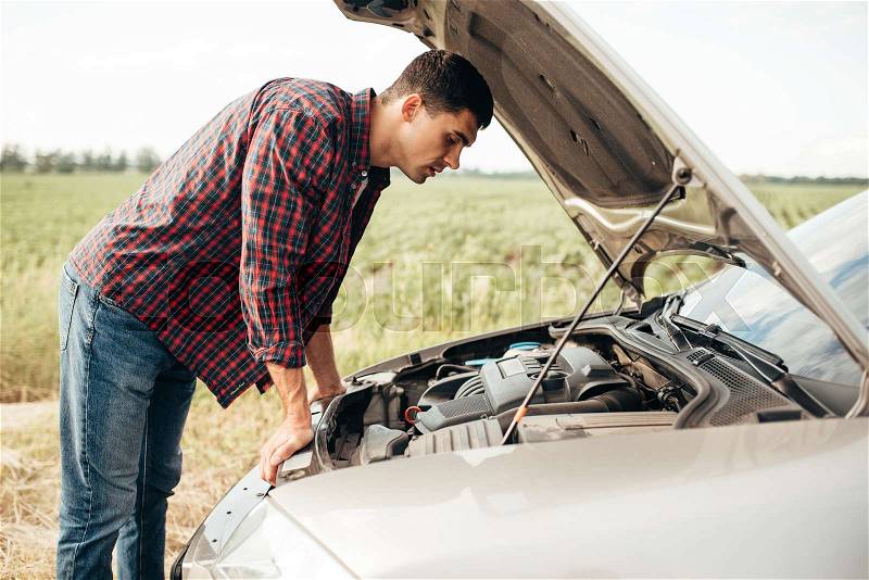 Tired man tries to repair a broken car. Vehicle with open hood on roadside, stock photo