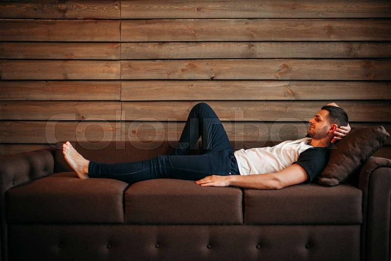 Young happy man lying on couch, side view. Relaxation on sofa. Male person relax, stock photo