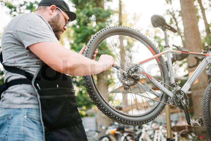 Bicycle mechanic repair bike, cycle workshop outdoor. Serviceman work with wheel and speed shifter, stock photo