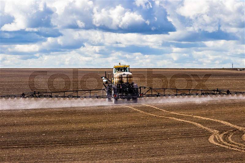Tractor spraying a field on farm, fertilizes the land, stock photo
