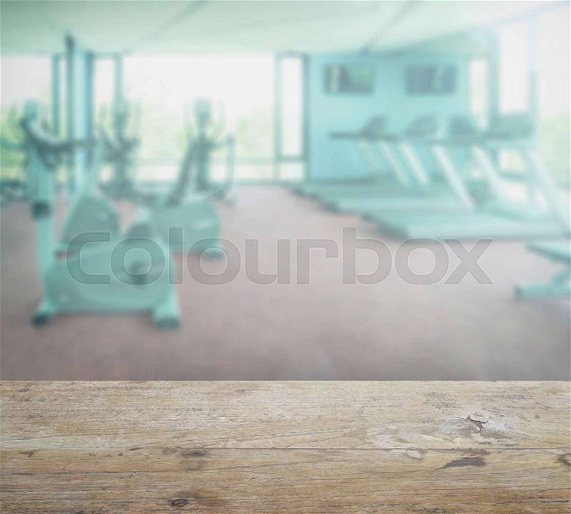 Wooden table top with blur of fitness room interior background, stock photo