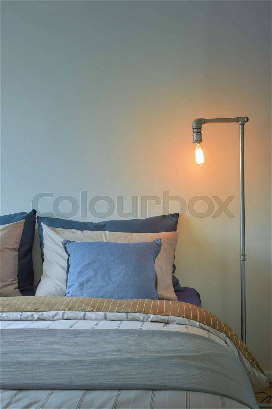 Industrial style reading lamp and blue pillows on modern style bedding, stock photo
