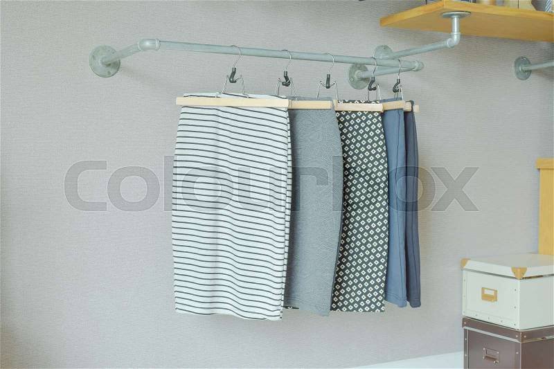 Skirts hanging on industrial style clothes rail in walk in closet, stock photo