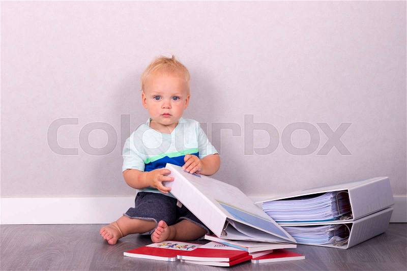 Funny toddler sitting on the floor with books and looking at camera, stock photo
