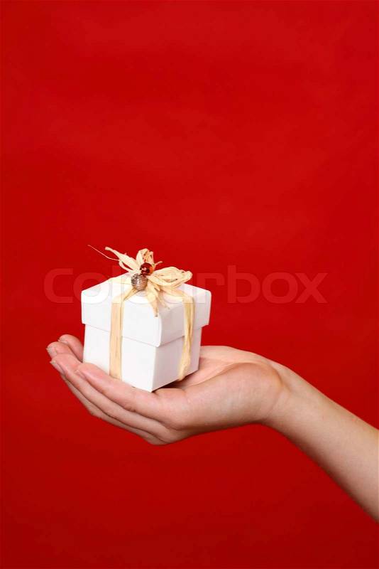 A wrapped and decorated giftbox in the palm of a hand against a red backdrop - suitable for Christmas, birthday or other special occasion, stock photo