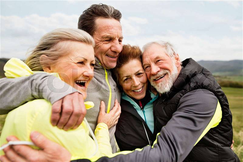 Group of active senior runners outdoors, resting and hugging in windy cold weather, stock photo