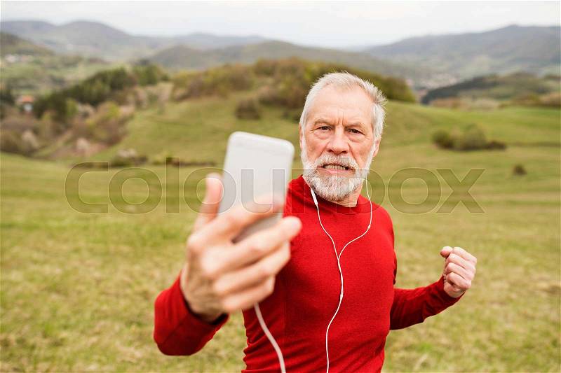 Active senior runner outside on the green hills taking selfie with smart phone, stock photo