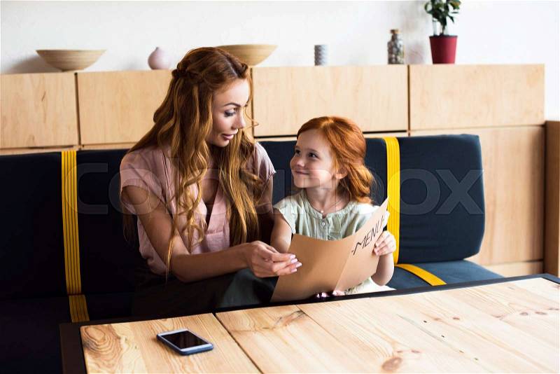 Beautiful smiling mother and daughter reading menu while sitting together in cafe , stock photo