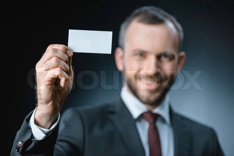 Selective focus of smiling businessman showing blank business card isolated on black, stock photo
