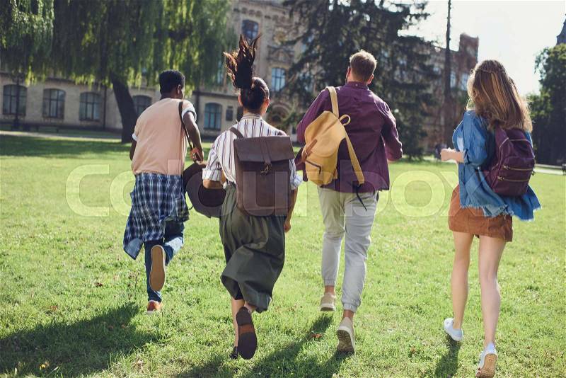 Back view of happy multicultural students running to college in park, stock photo