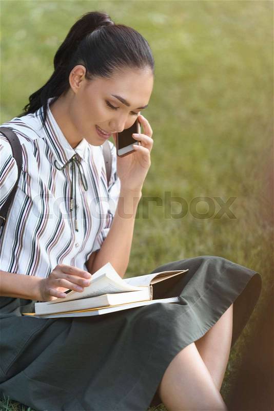 Attractive female asian student with smartphone reading book, stock photo