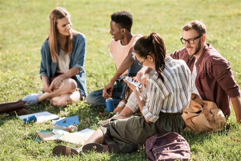 Young multiethnic group of students studying together while sitting on green grass, stock photo