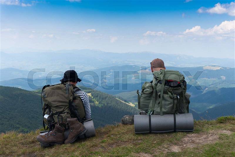 Two tourists sitting on a cliff against a background of mountains, stock photo