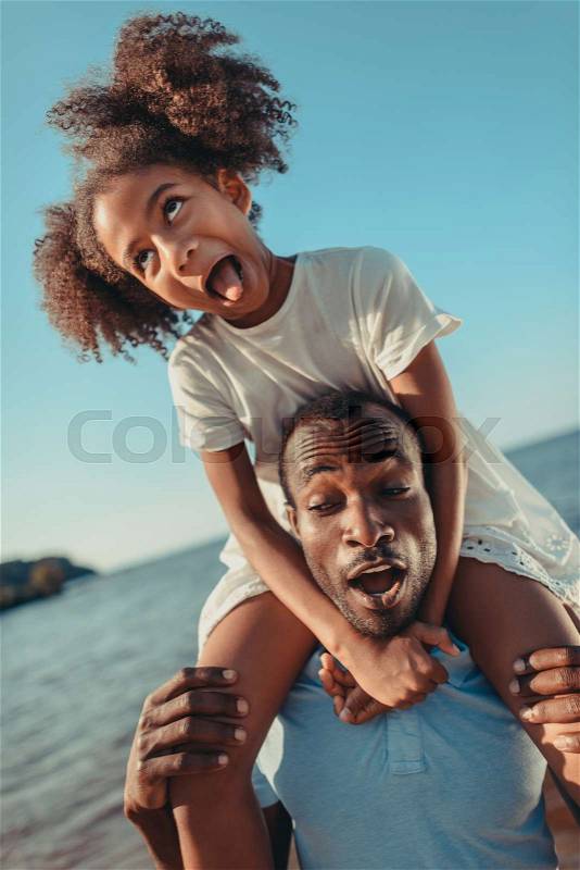 Funny african american father and daughter having fun together at seaside, stock photo