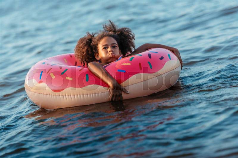 Cute african american girl swimming in rubber ring and smiling at camera, stock photo
