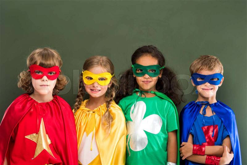 Little pupils in colorful superhero costumes, chalkboard behind, stock photo