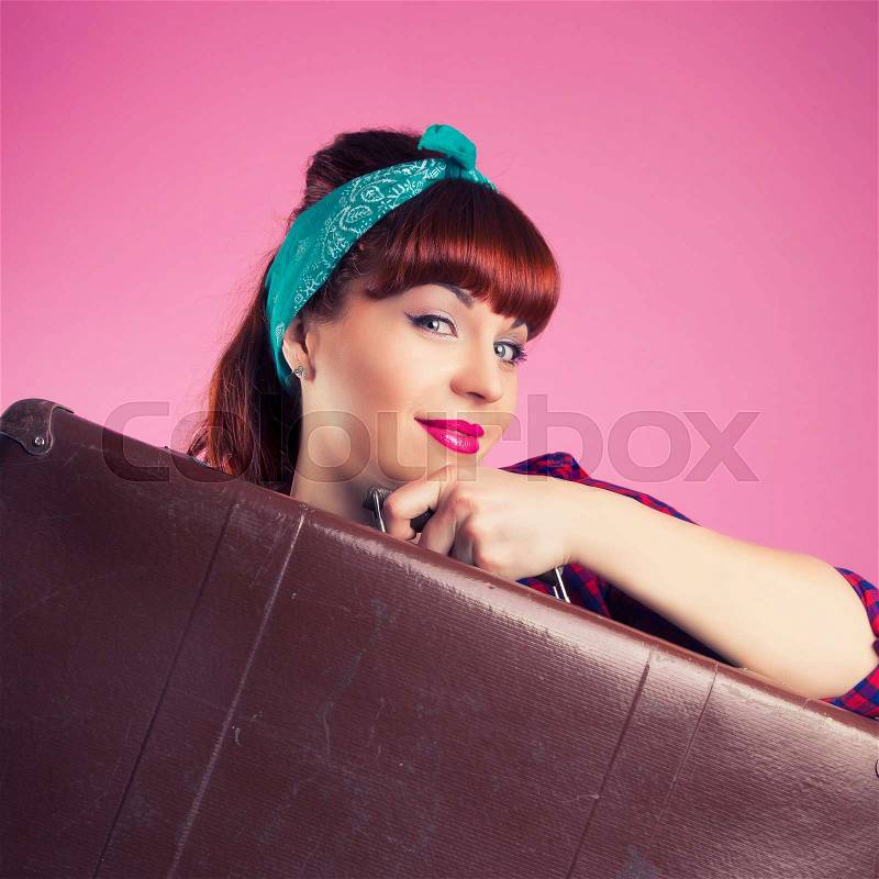 Beautiful pin-up girl posing with vintage suitcase against pink background, stock photo