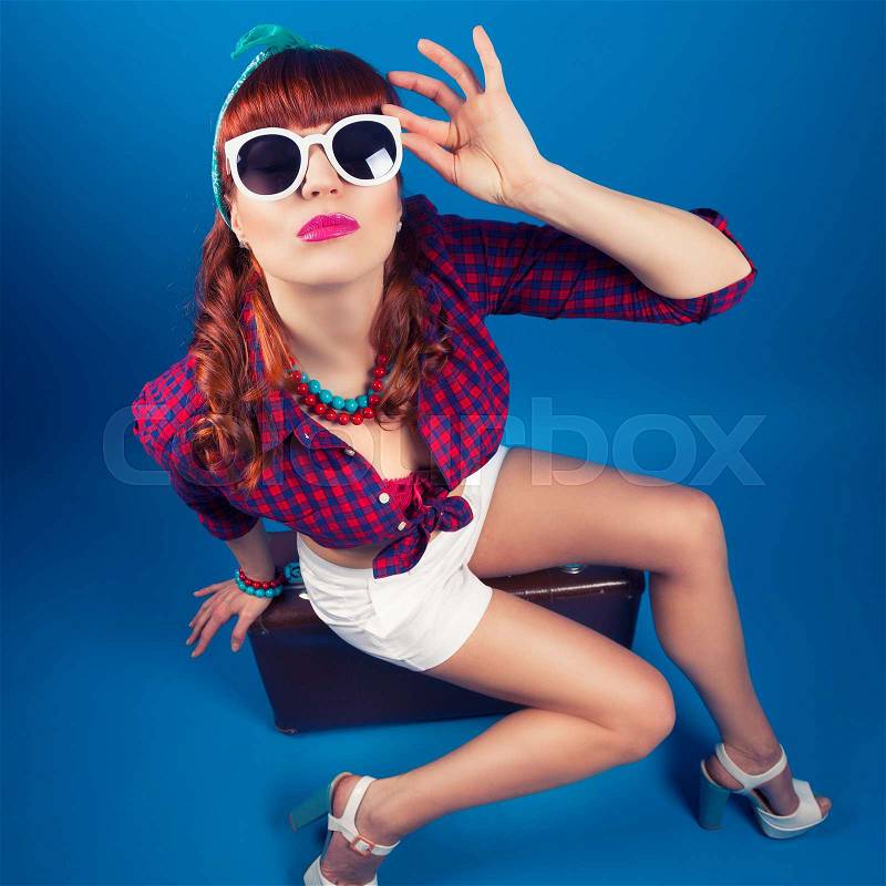 Beautiful pin-up girl posing with vintage suitcase against blue background, stock photo