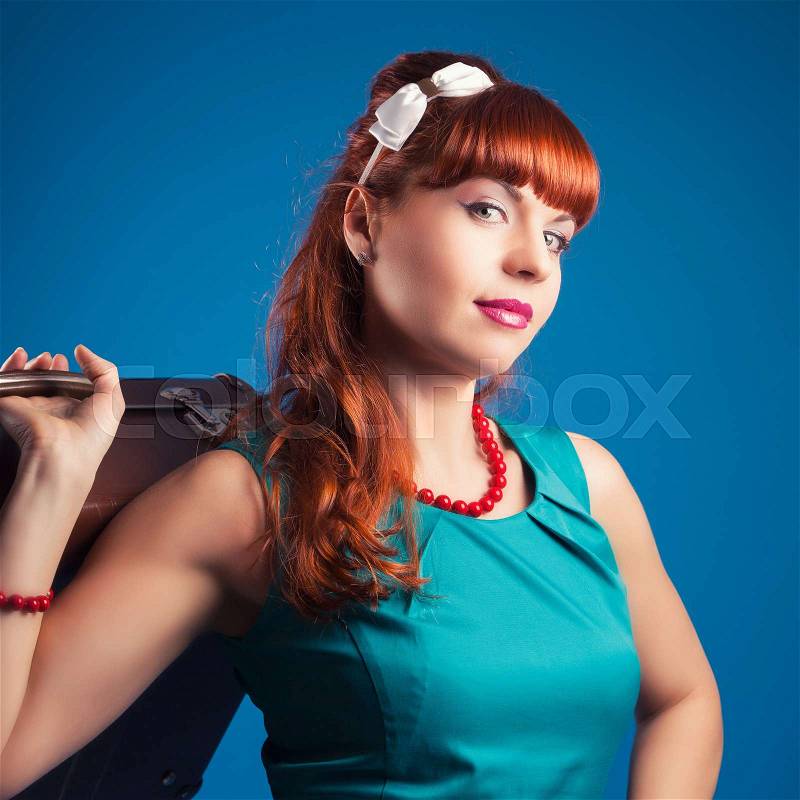 Beautiful pin-up girl posing with vintage suitcase against blue background, stock photo