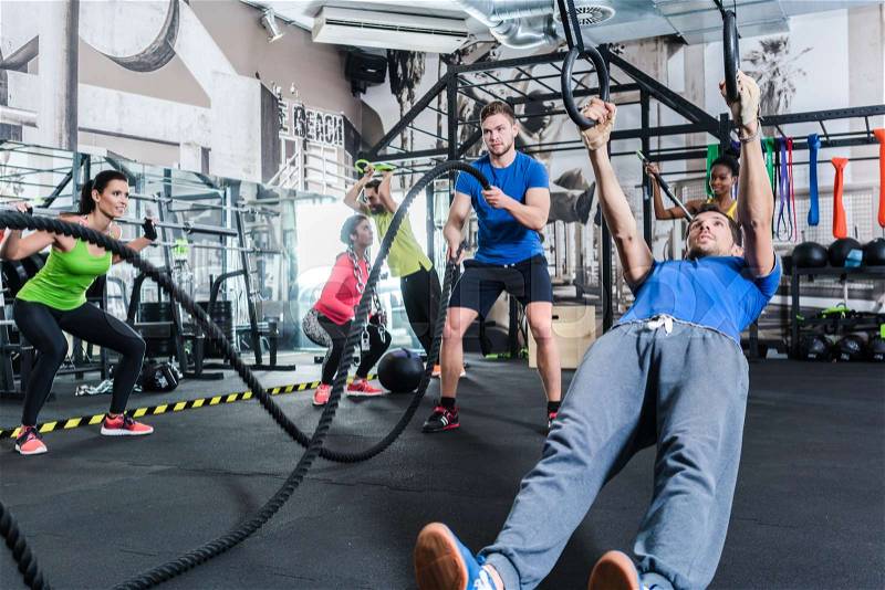 Men and women at functional fitness training in gym doing sport on rings and rope, stock photo