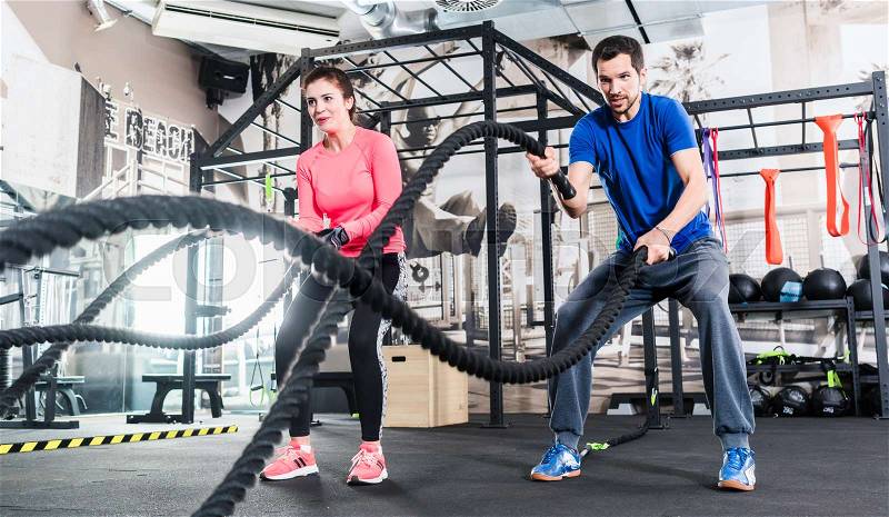 Woman and man in gym functional training with battle rope exercising, stock photo