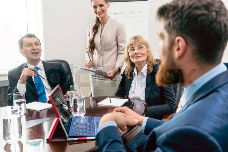 Happy middle-aged managers listening to their younger colleague while planning business in the conference room of a successful corporation, stock photo