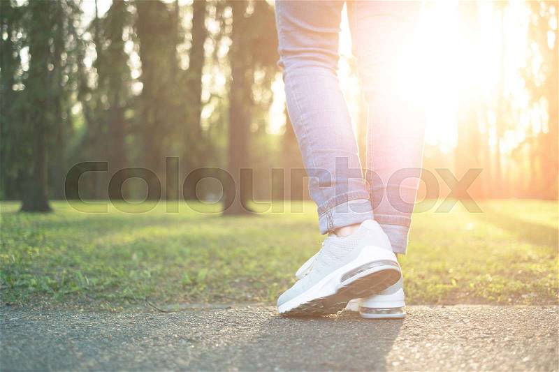 Person walking in nice gray comfortable running shoes in the green park in sunlight, closeup, stock photo