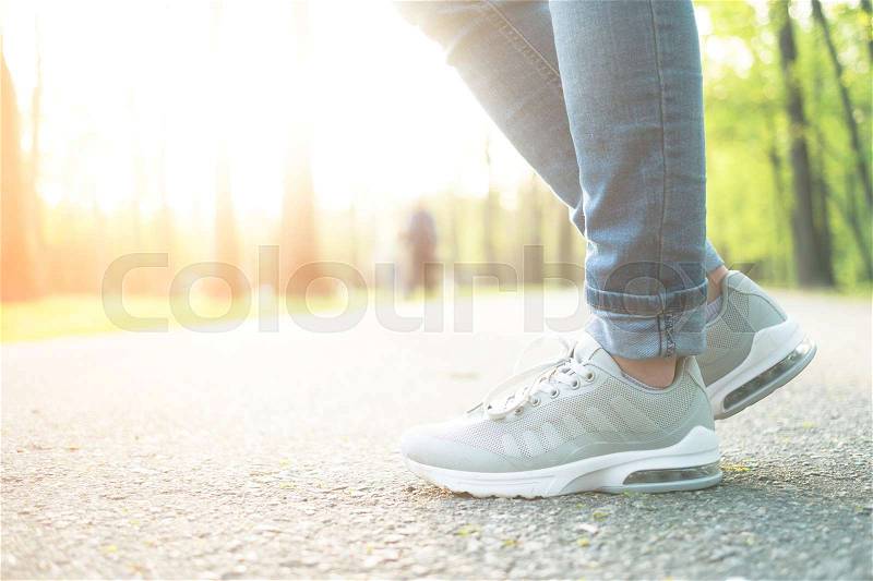 Person standing in blue designed jeans and gray sporty gumshoes with white soles, outdoors, stock photo