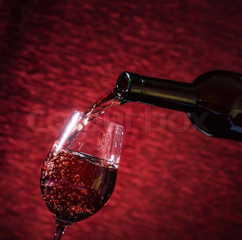 Red wine pouring into the glass from the bottle. Red background. The concept of a holiday, celebrations, stock photo