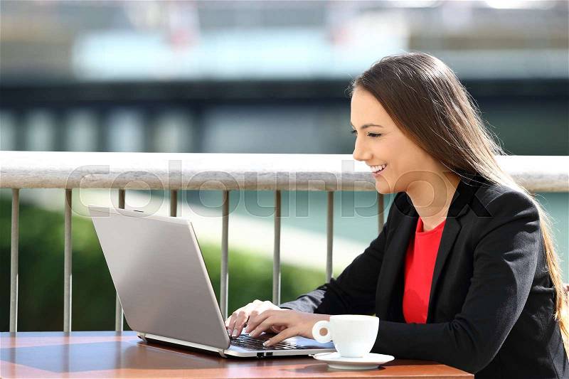 Single happy executive typing in a laptop sitting in a coffee shop, stock photo