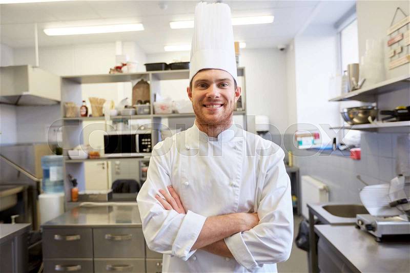 Cooking, profession and people concept - happy male chef cook in toque with crossed hands at restaurant kitchen, stock photo