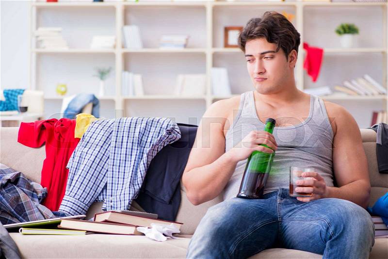 Young man student drunk drinking alcohol in a messy room, stock photo
