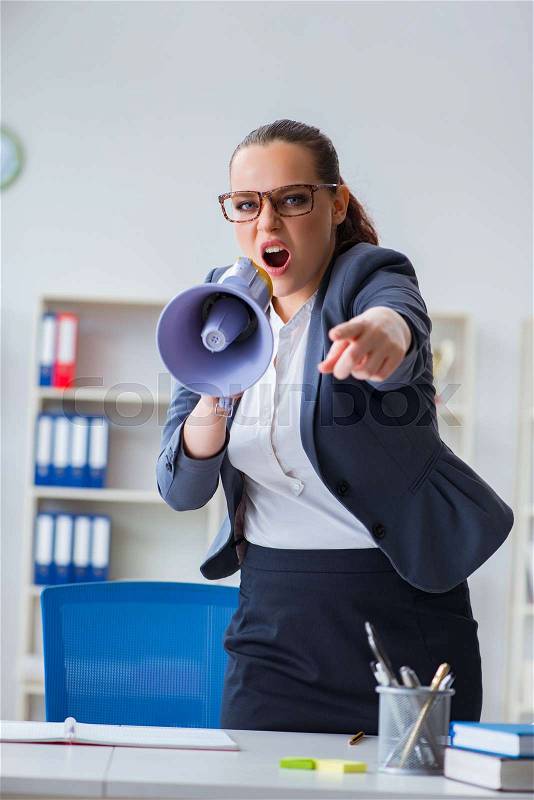 Angry businesswoman yelling with loudspeaker in office, stock photo