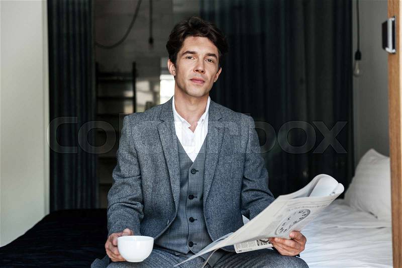 Businessman with coffee cup reading newspaper at a hotel room, stock photo