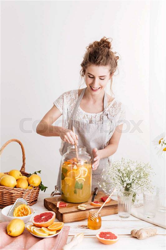 Image of amazing concentrated woman standing indoors cooking citrus beverage. Looking aside, stock photo