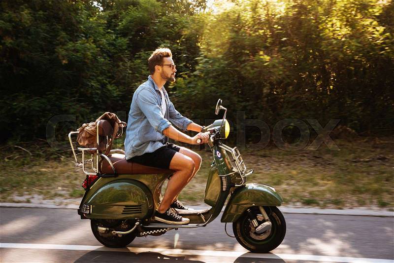 Image of serious young bearded man on scooter outdoors. Looking aside, stock photo