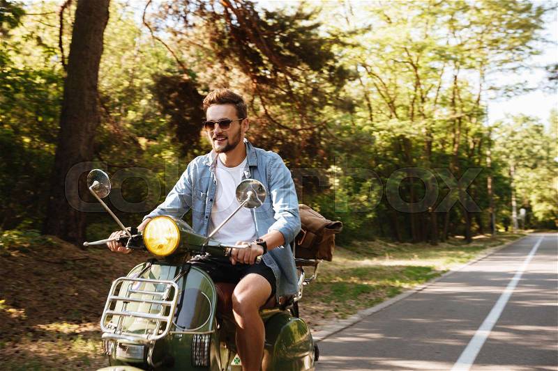 Image of serious young bearded man on scooter outdoors. Looking aside, stock photo