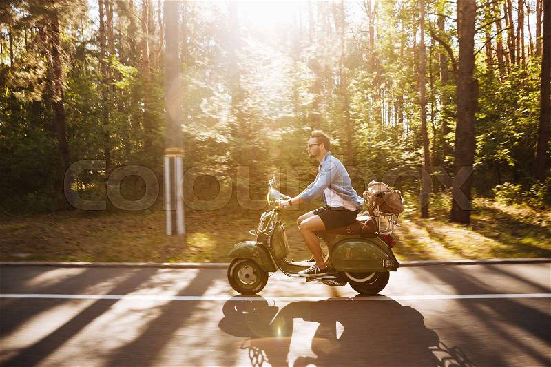 Picture of young bearded man on scooter outdoors. Looking aside, stock photo