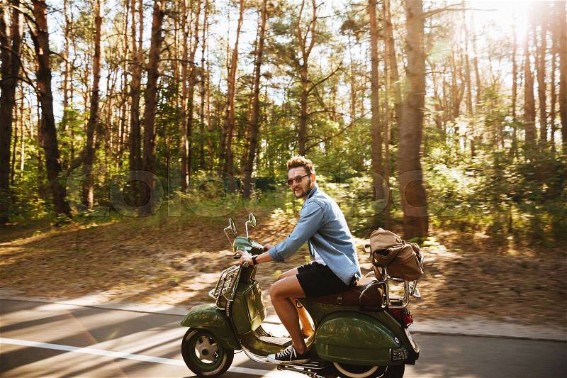 Picture of young bearded man on scooter outdoors. Looking camera, stock photo